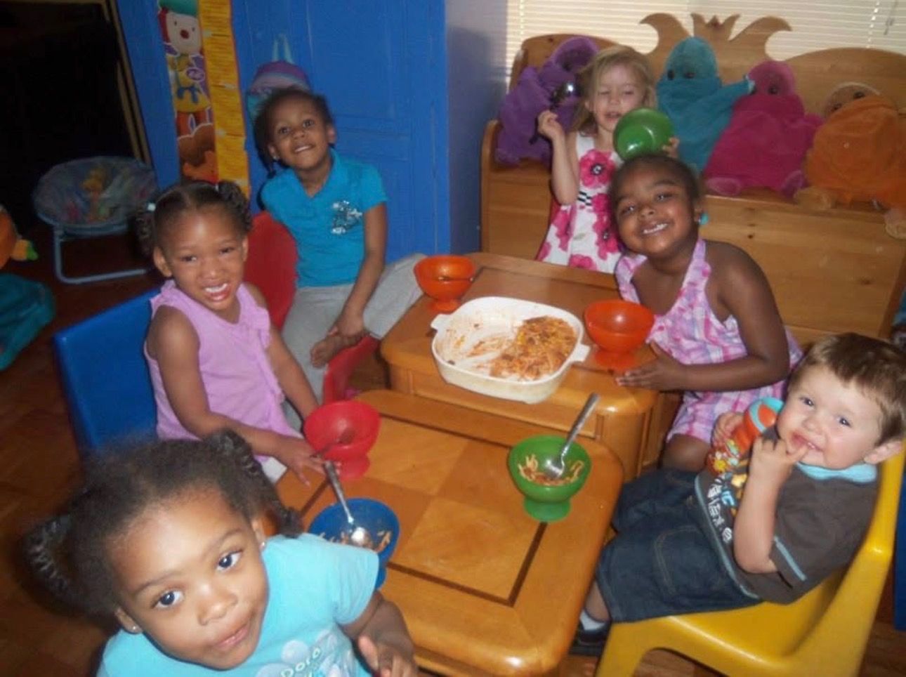 Children seated around a small table with snacks in a cozy living room, smiling at the camera