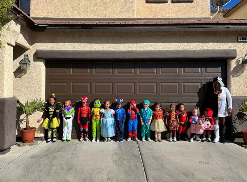 A row of children in colorful costumes standing in front of a garage door on a sunny driveway