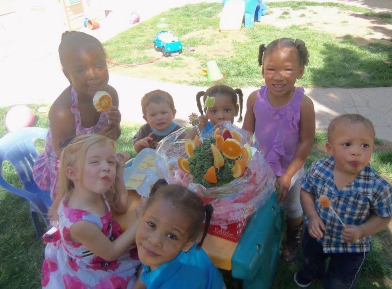 Children gathered around a decorated birthday table outdoors, smiling and holding toys.