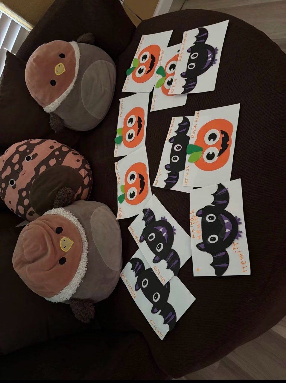 Halloween paper crafts on a dark table: two yarn pumpkins, a bat garland, and a folded bat-pop-up card.