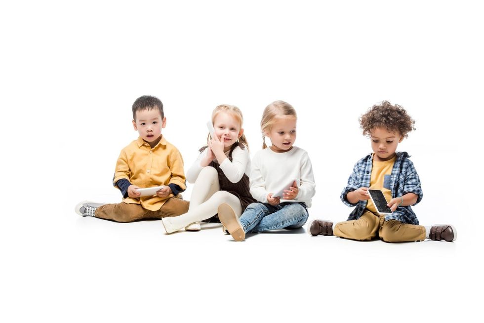 Four children sitting cross-legged on a white background, playing with toy blocks.
