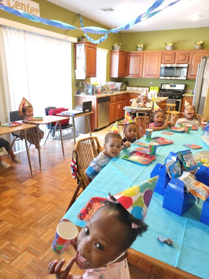Children seated at a long birthday table in a bright kitchen, with party hats, snacks, and decorations.