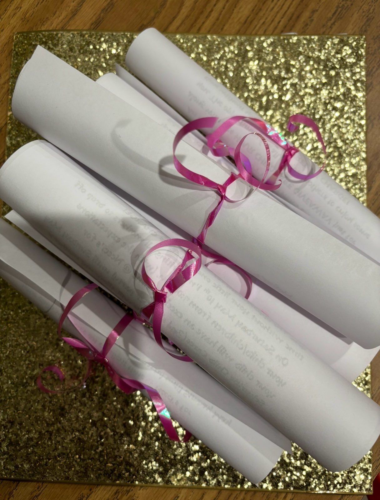 Rolled white papers tied with pink ribbon on a gold glitter background