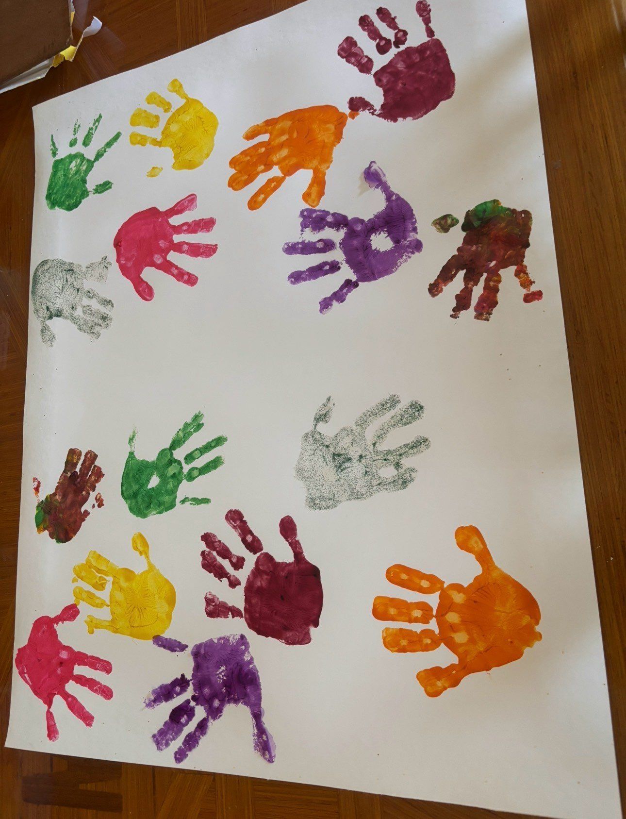 Colorful painted handprints on white paper, arranged in a scattered pattern.