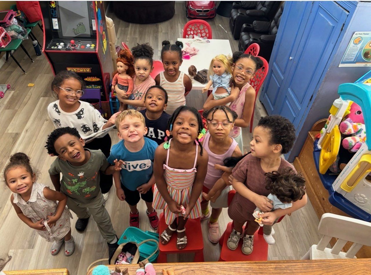 Group of children standing indoors and smiling up at the camera in a classroom or playroom.