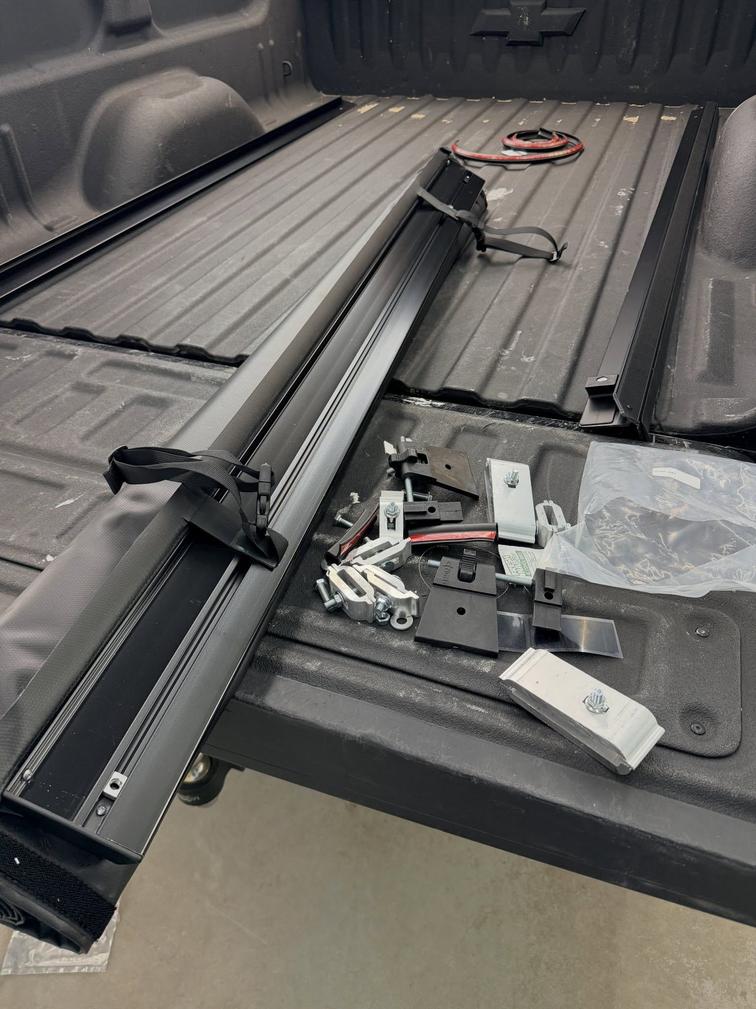Black metal bed frame parts and hardware laid out in a pickup truck bed, with a red cord in the corner