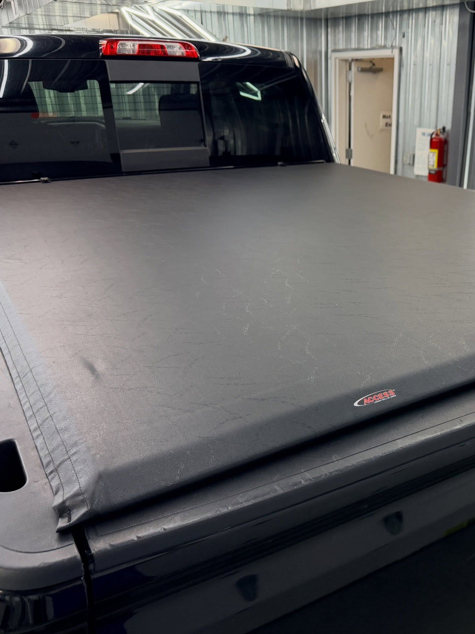 Black pickup truck with a textured tonneau cover parked inside a garage