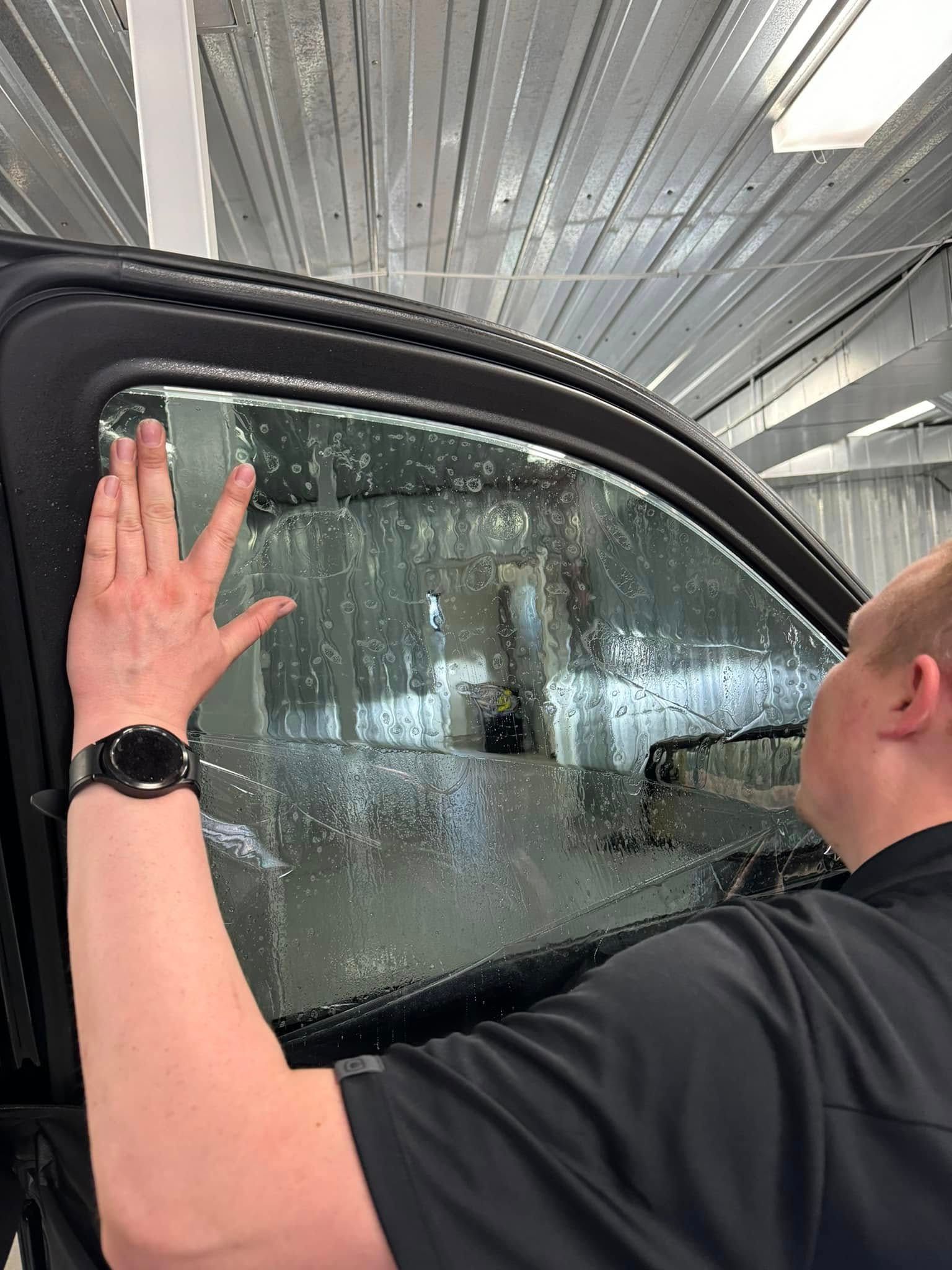Person washing a car window at an automatic car wash, hand pressed against a soapy pane.