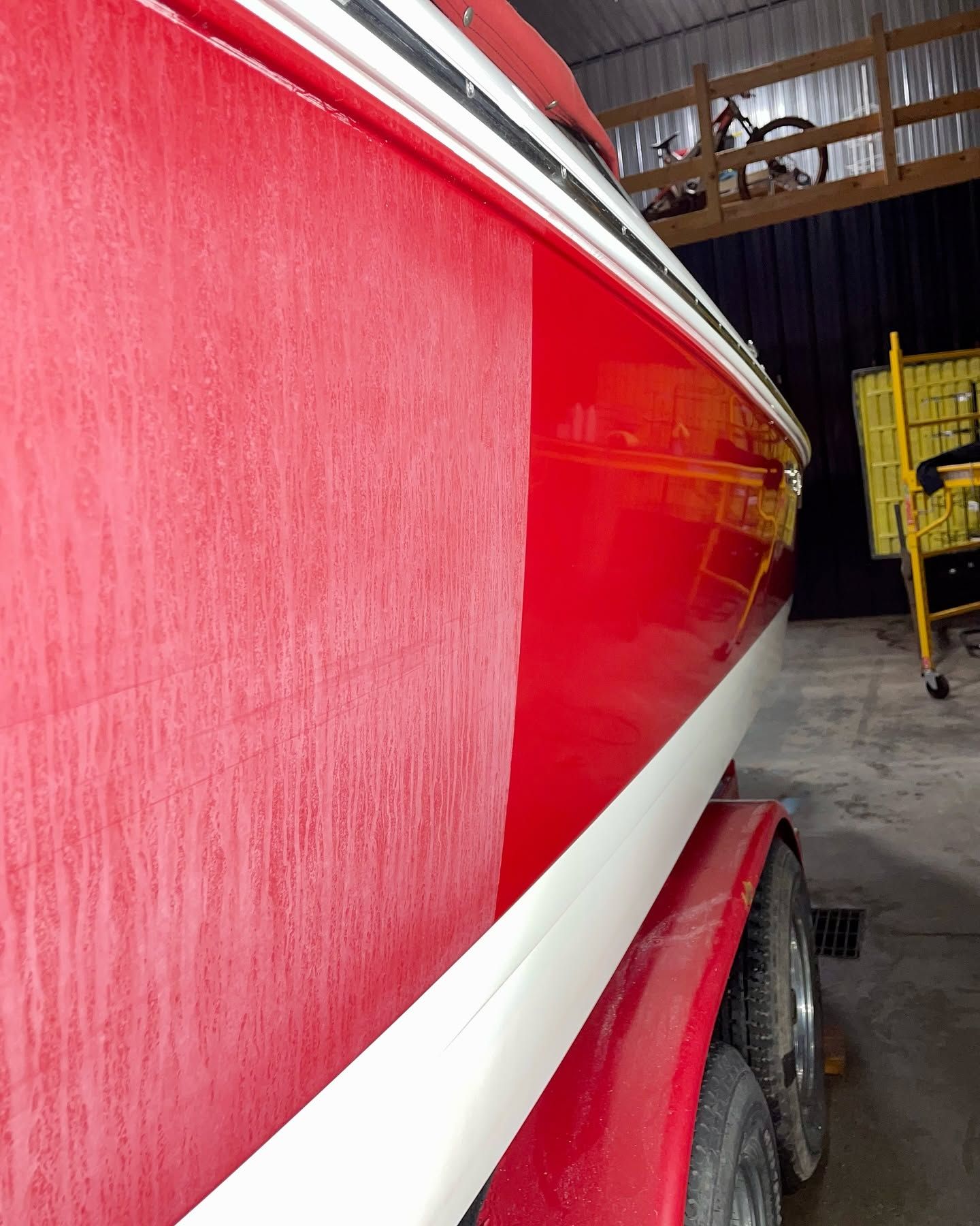 Red boat hull with white stripe inside a workshop, close-up view