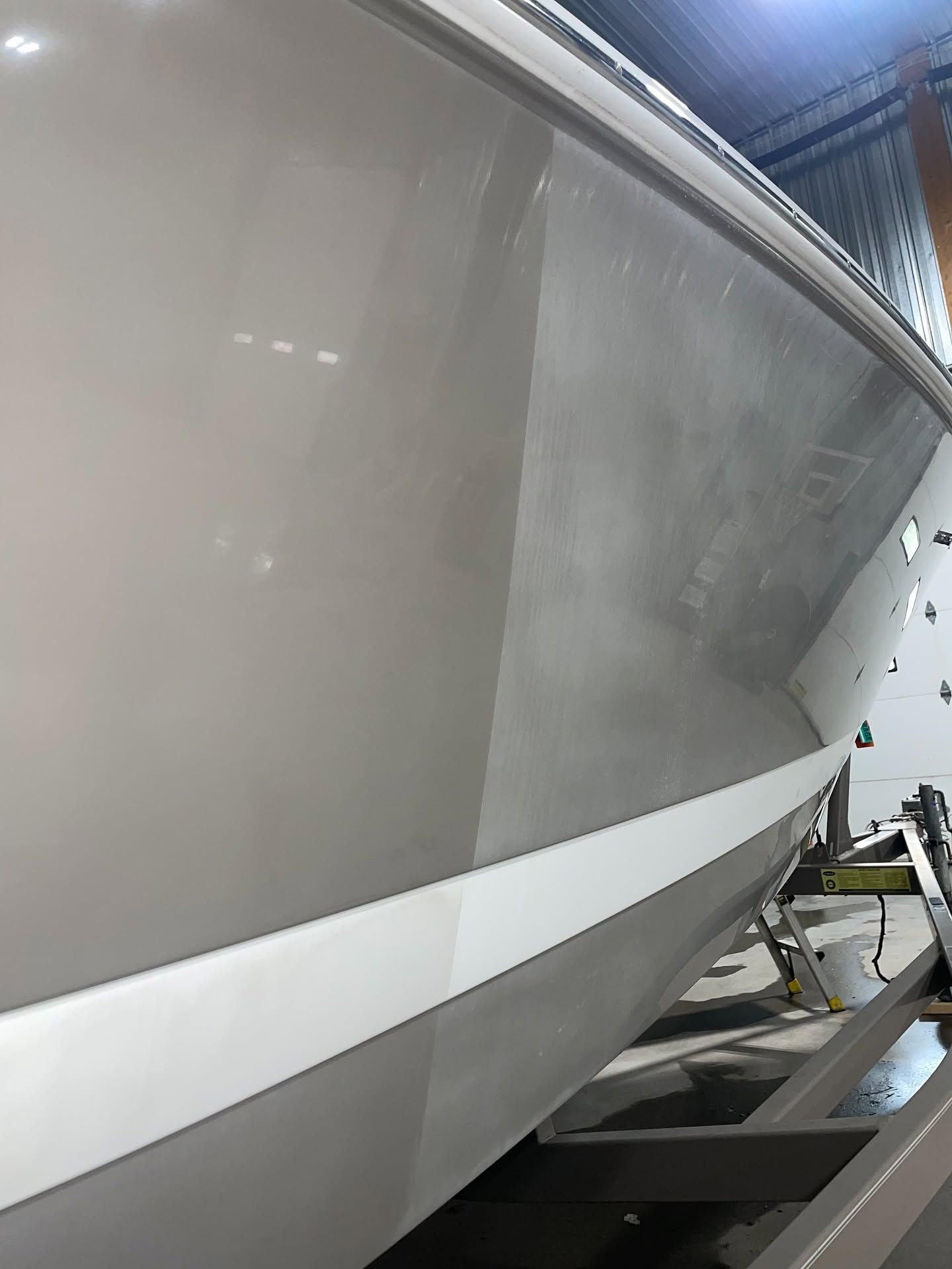 Close-up of a gray sailboat hull with a white stripe in a boatyard or workshop