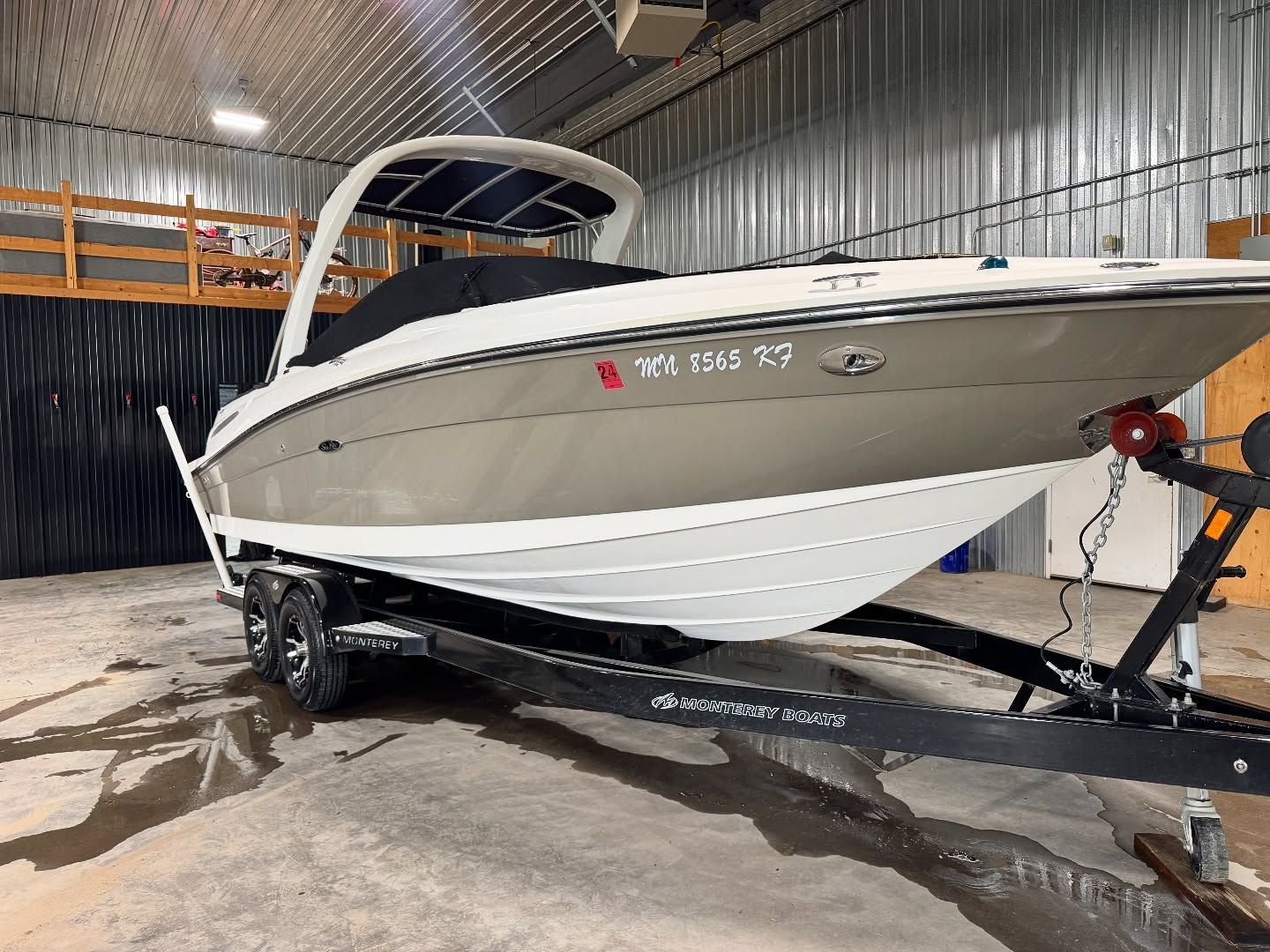 White speedboat on a trailer in a covered storage area, with wet floor and dock equipment nearby