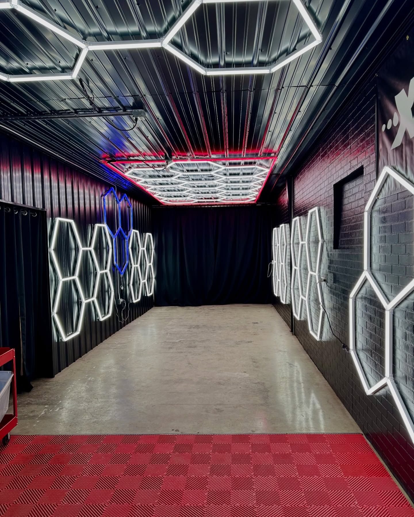 Futuristic hallway with glowing hexagonal LED wall and ceiling panels, red carpet, and black draped end wall