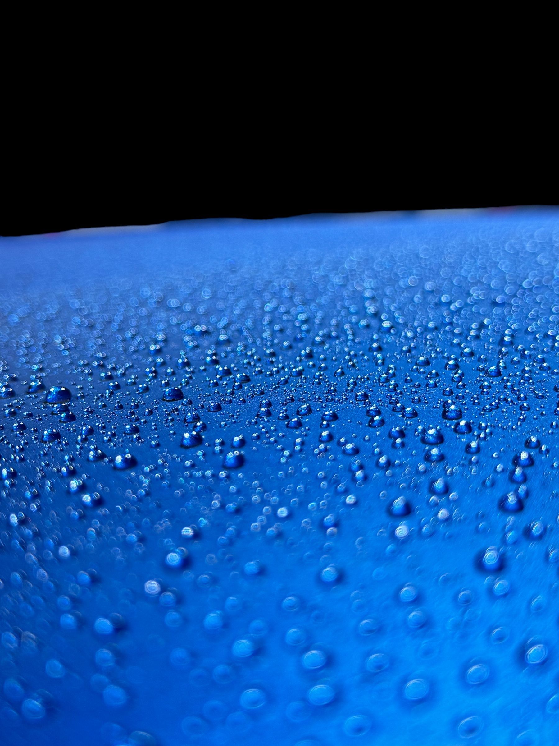 Blue surface covered with water droplets against a black background