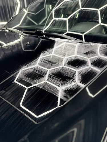 Geometric white light pattern reflected on a glossy black car hood and windshield