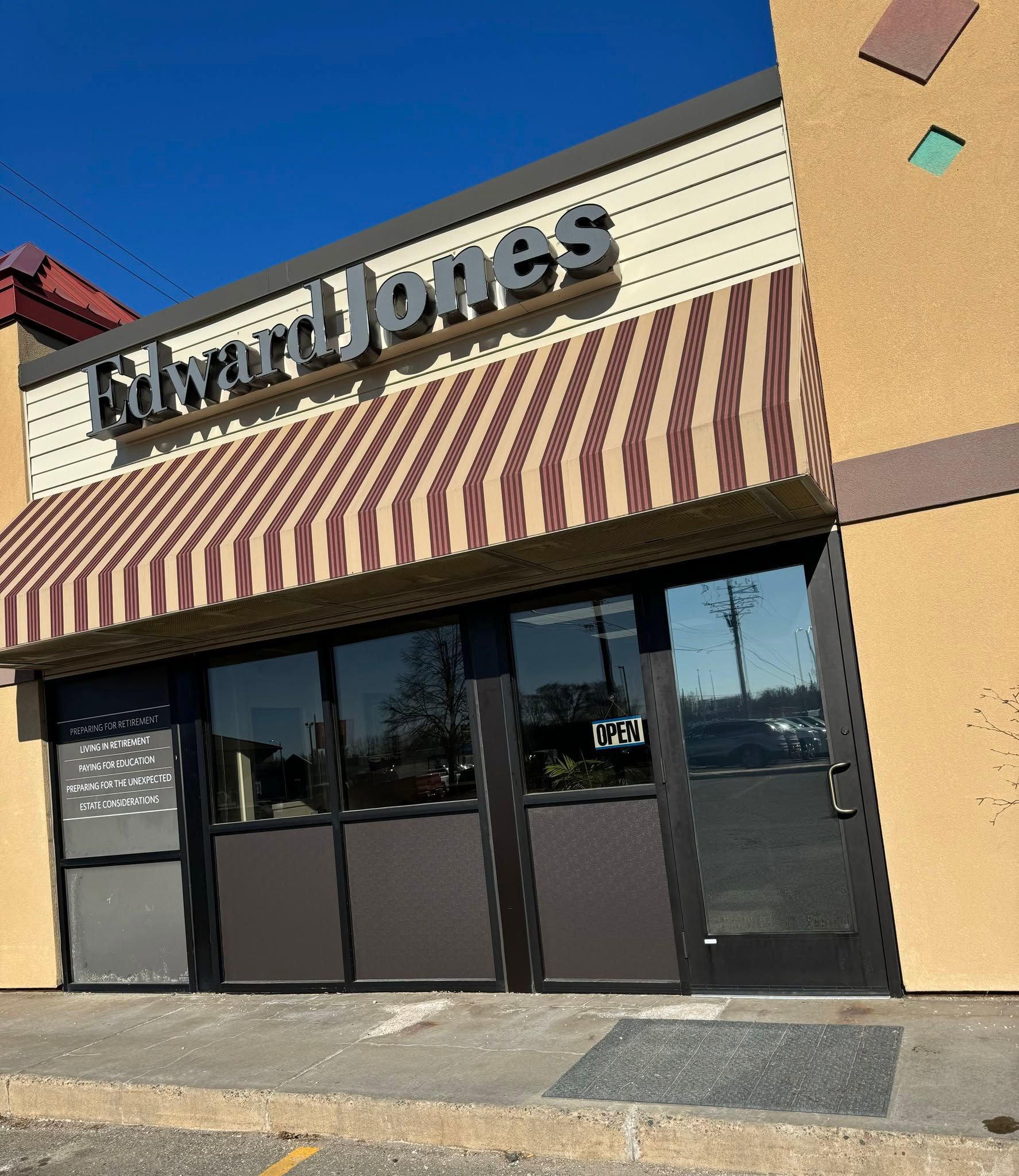 Storefront with striped awning and large glass doors under a sign on a beige building exterior