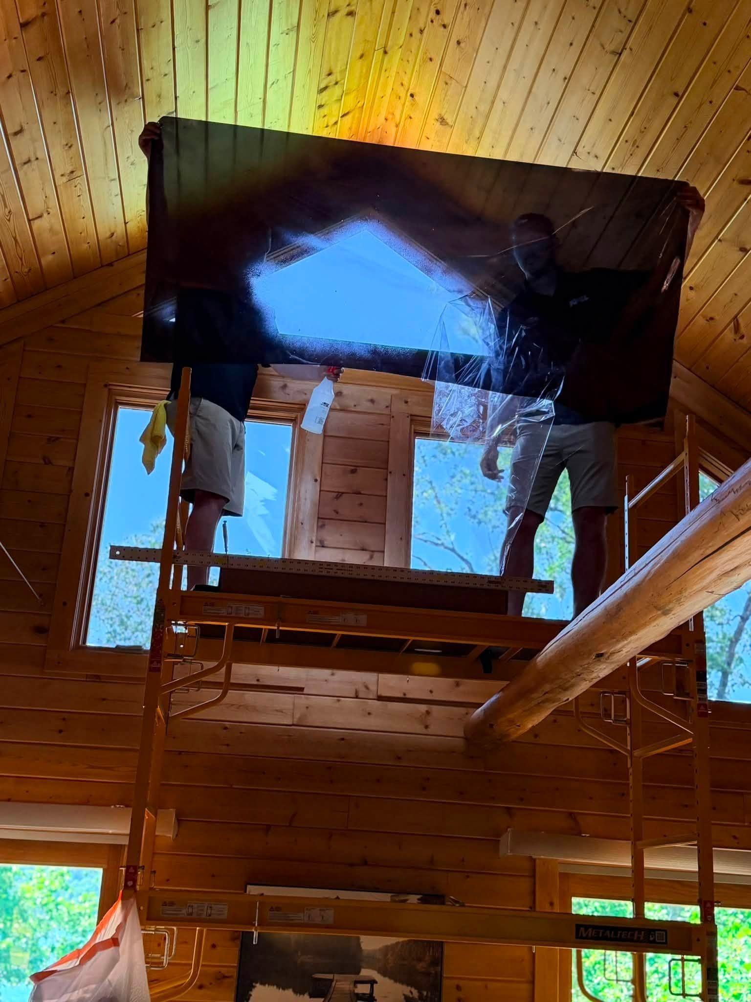 Interior of a rustic wooden cabin with a loft, stair railings, and a bright roof opening above.