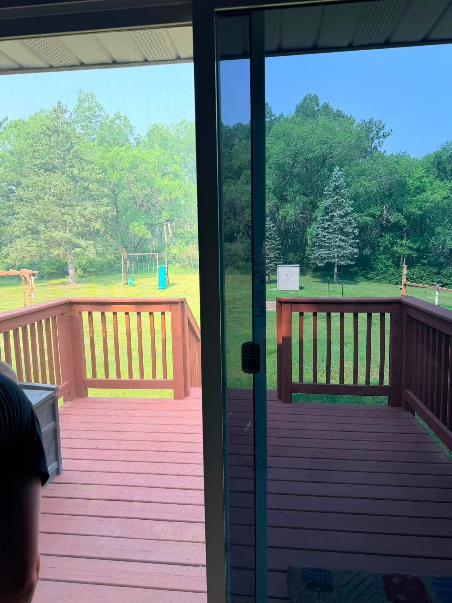 Backyard deck with red railing, sliding glass door, and green trees in the distance