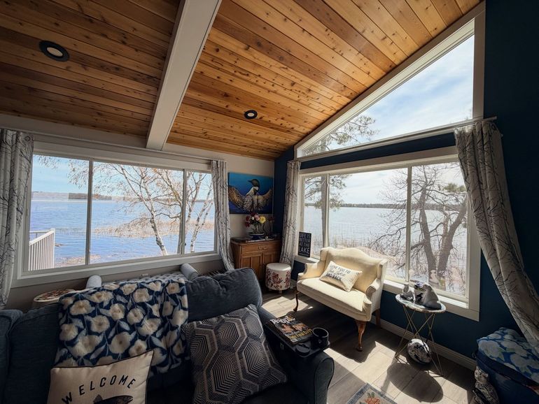 Cozy cabin living room with large windows, wood-paneled ceiling, and a lake view