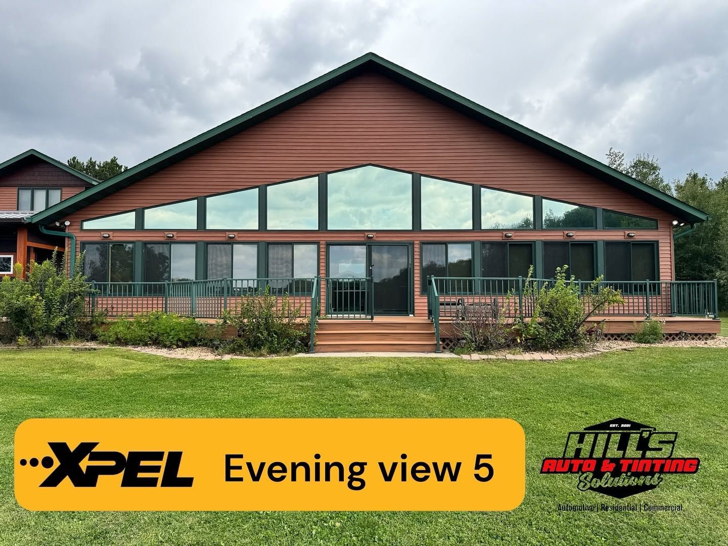 Wooden lodge with large windows and covered porch, labeled “XPEL Evening view 5” under cloudy skies