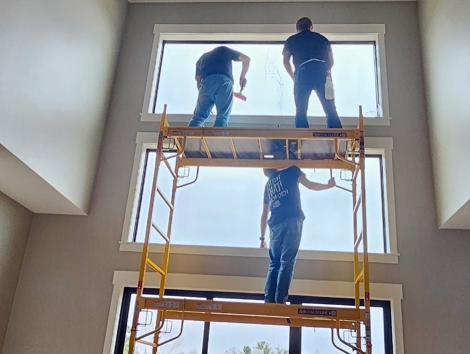 Three workers on scaffolding installing a large window in a bright interior.