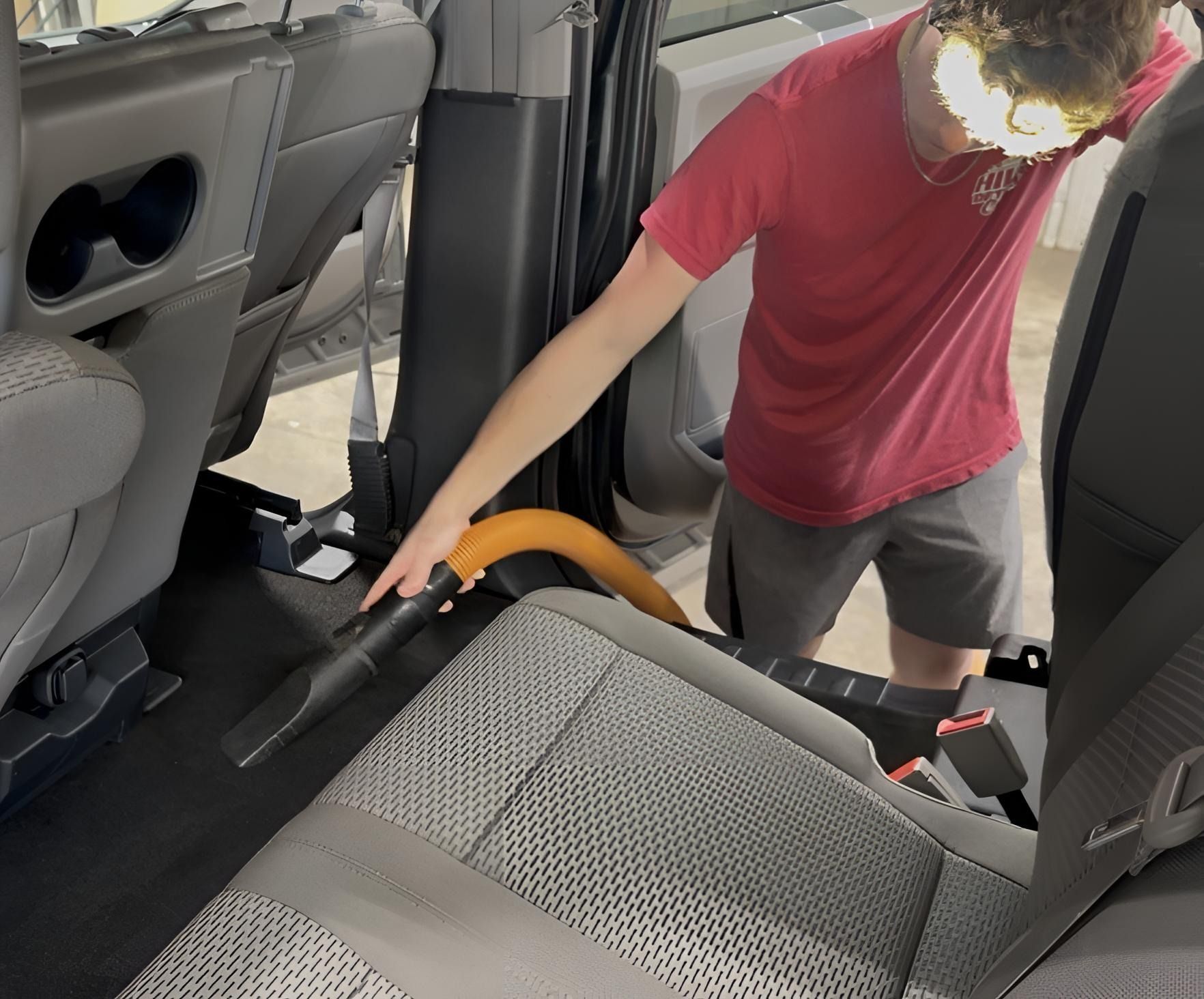 Person vacuuming car interior with an orange hose, cleaning the back seat area.
