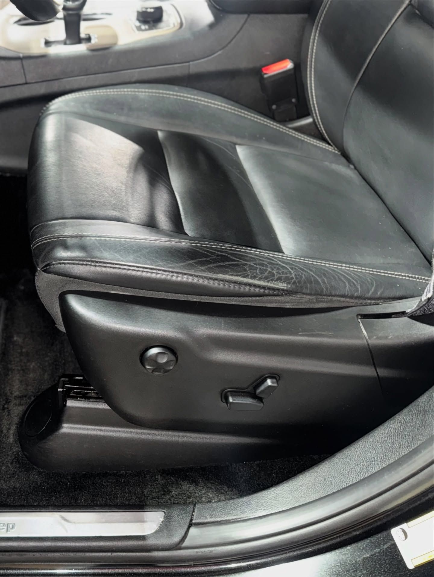 Black leather car seat with side adjustment controls and stitching detail in a vehicle interior
