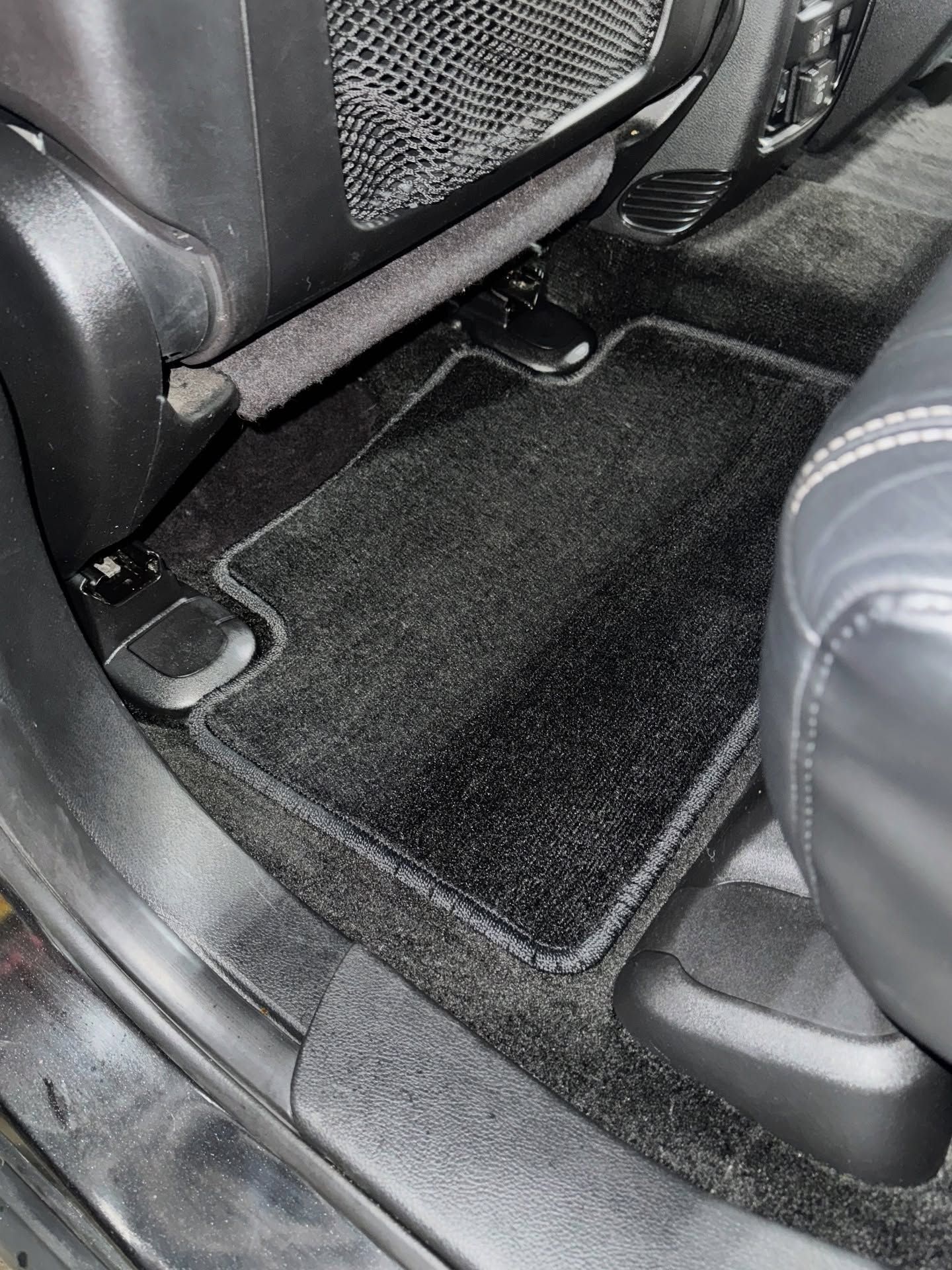 Car interior with a black floor mat between two seats, viewed from the rear seat area