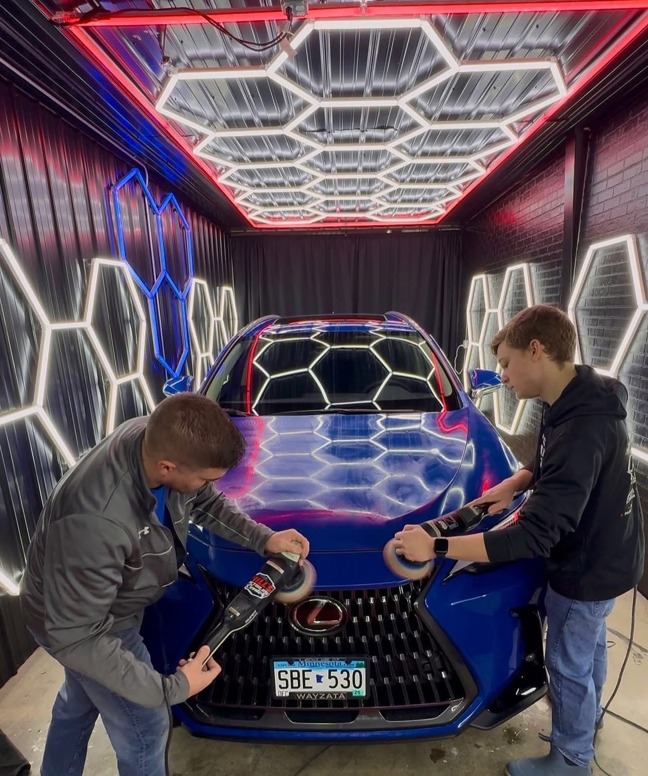 Two people inspecting a blue car in a neon-lit display tunnel