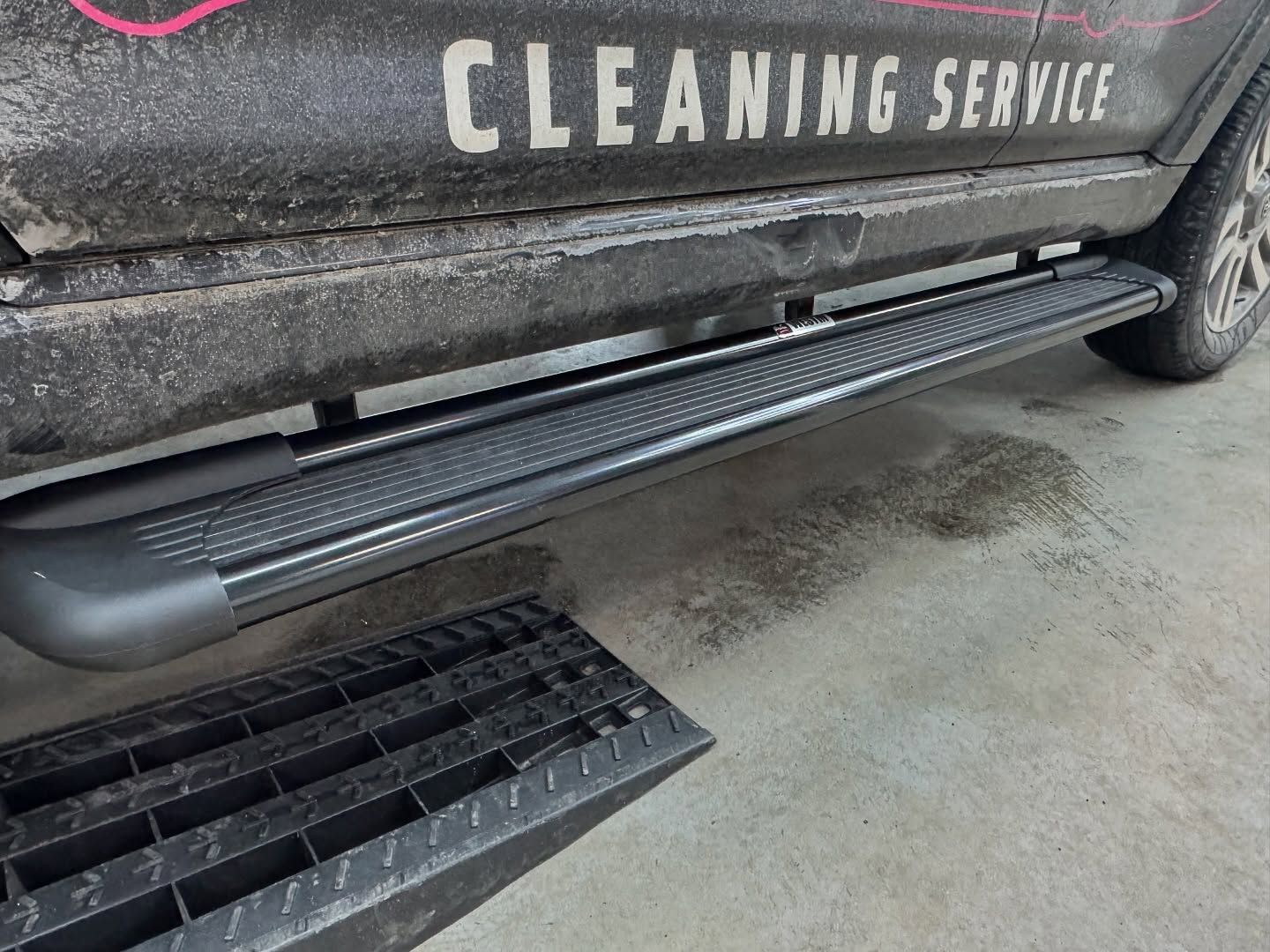 Side view of a cleaning service van with a deployed black step/ramp on a concrete floor.