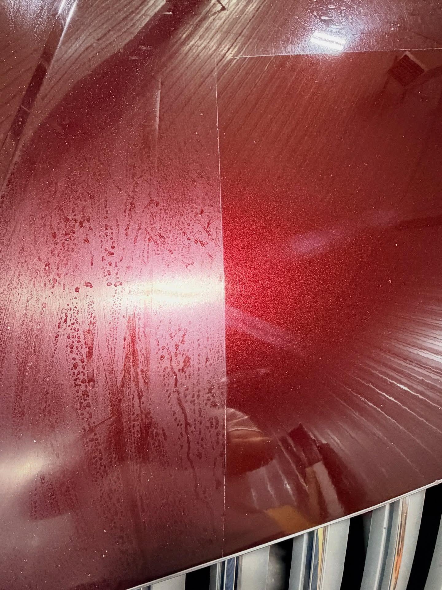 Close-up of a scratched red car body with a bright reflection and water droplets