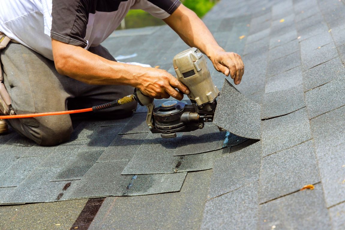 Worker using a power tool to cut shingles on a roof during repairs
