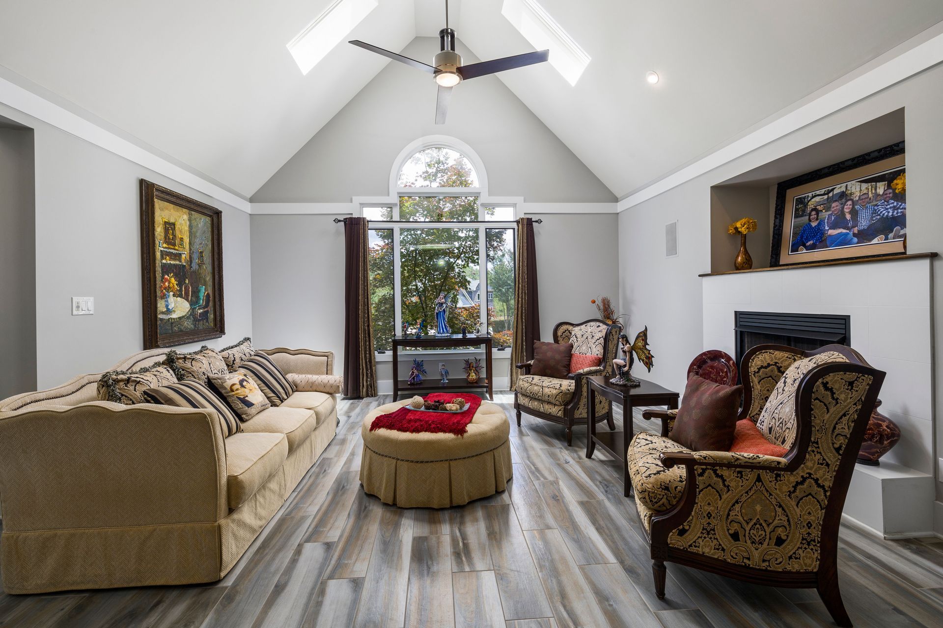 Elegant gray living room with vaulted ceiling, patterned chairs, sofa, and large arched window