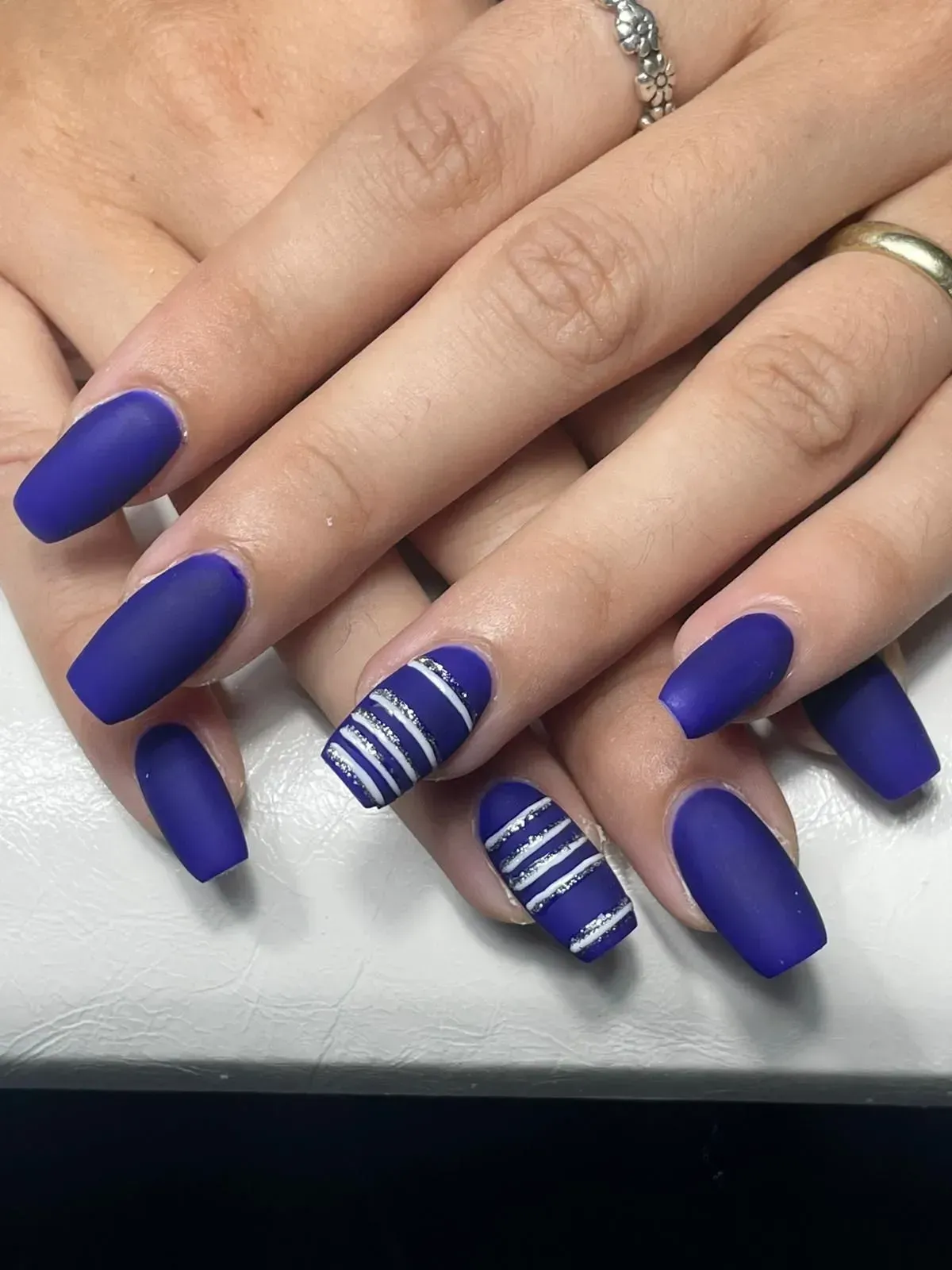 Mani con unghie lunghe color blu cobalto opaco; due unghie decorative presentano strisce bianche.