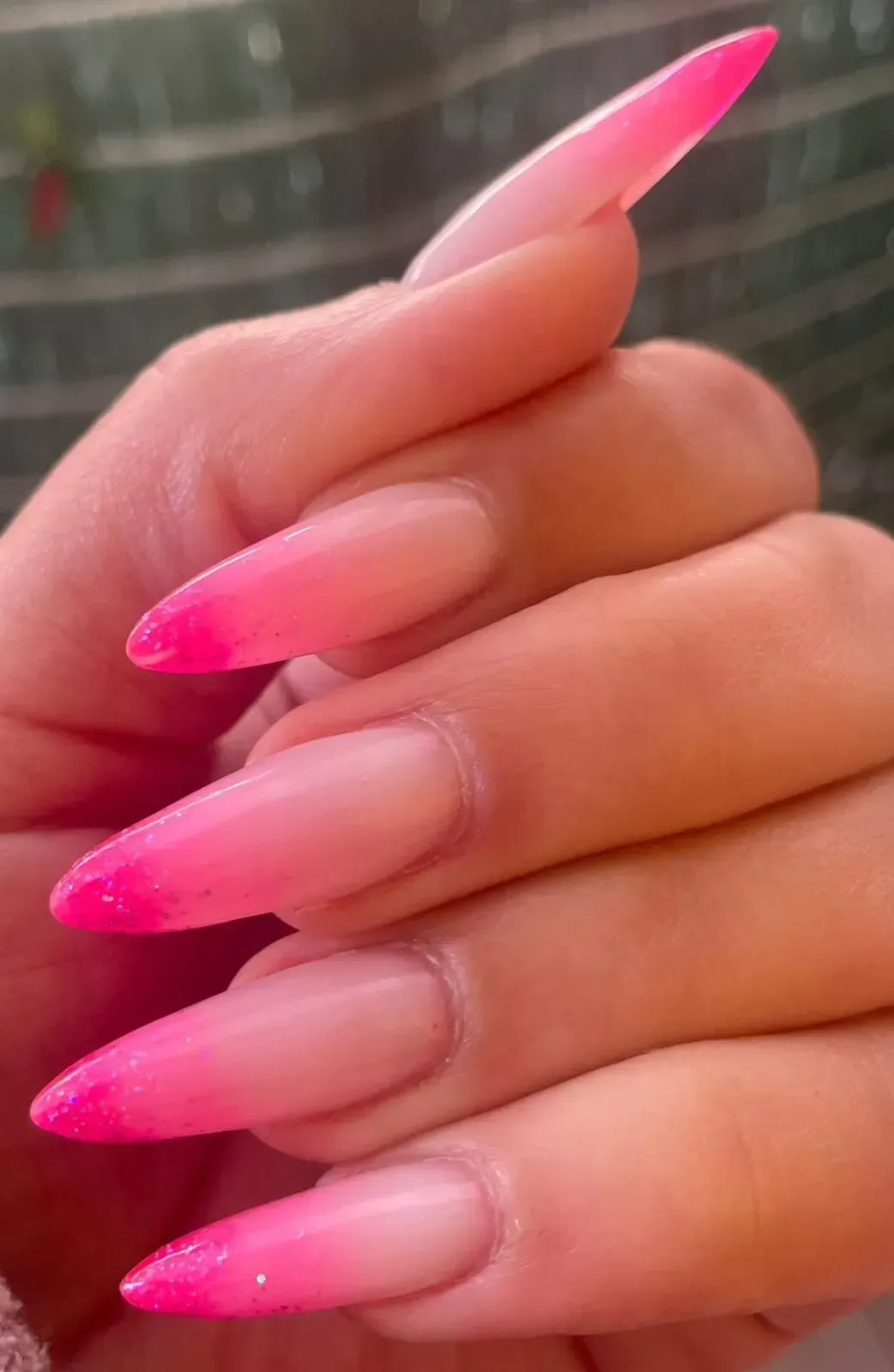 Primo piano di lunghe unghie acriliche rosa sfumate con punte glitterate