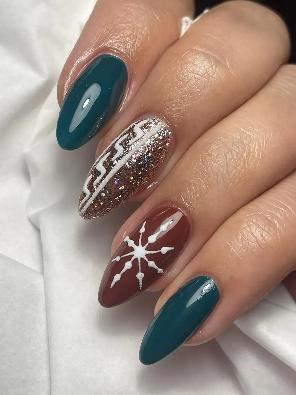 Mano con manicure color verde acqua e bordeaux, un'unghia con glitter e nail art a forma di stella bianca.