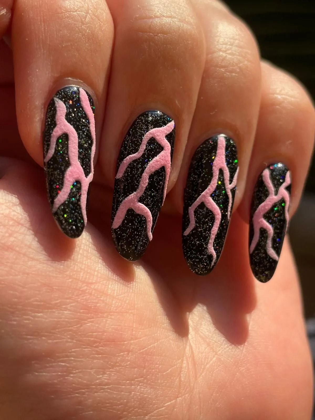 Mano con lunghe unghie nere glitterate con un disegno ondulato rosa e decorazioni di strass