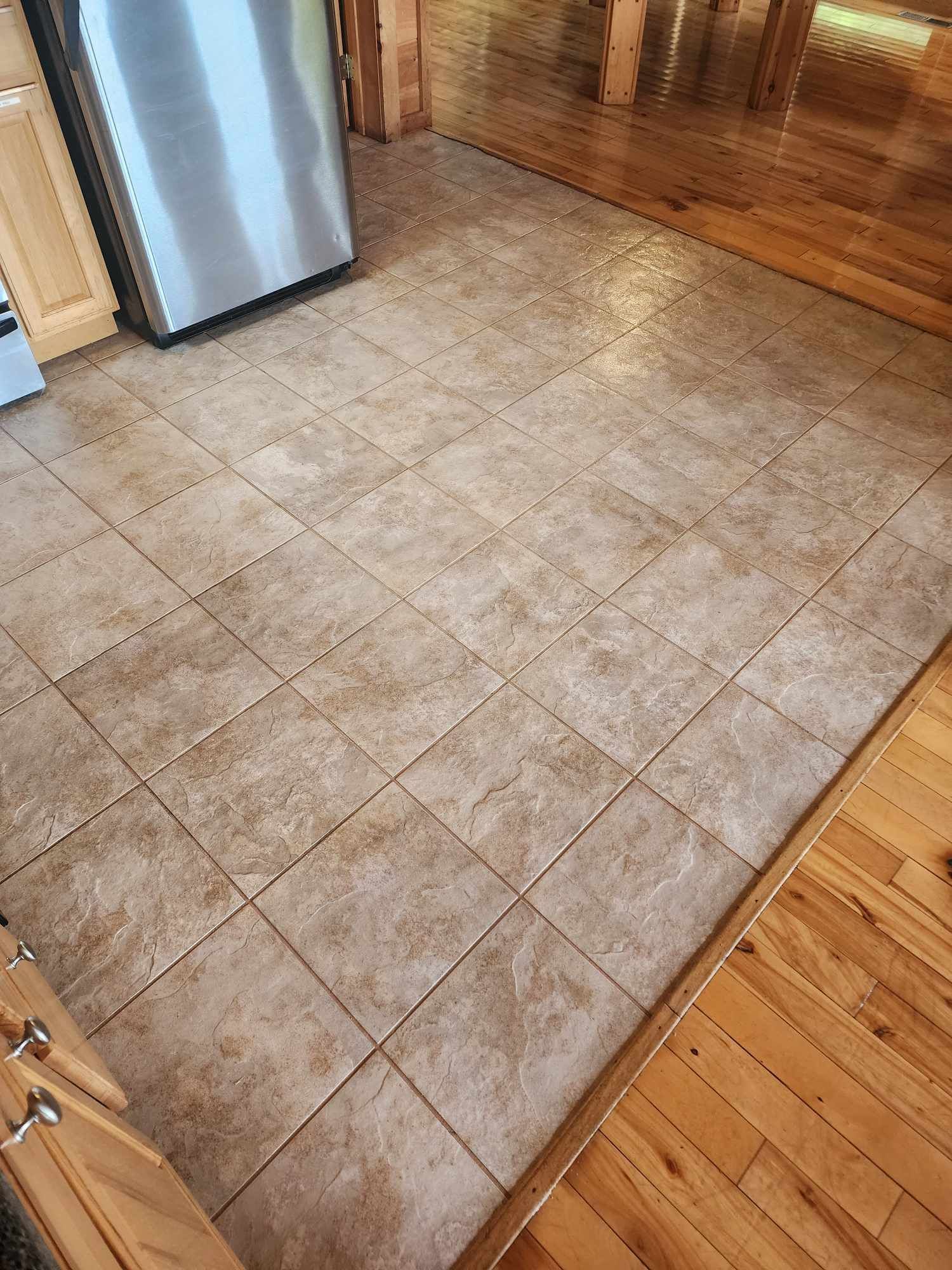A kitchen floor with tiles and wooden floors and a stainless steel refrigerator.