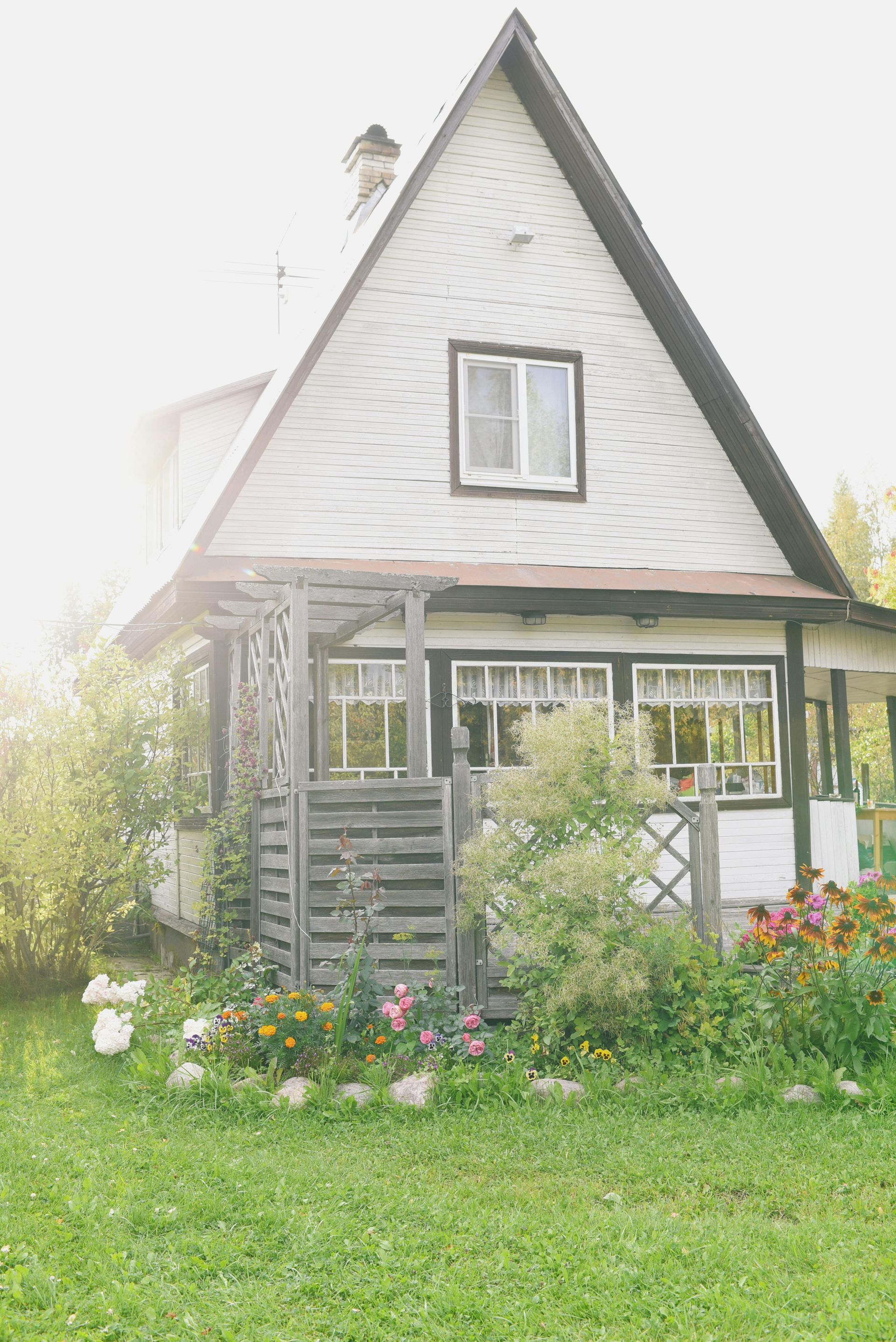 A small white house with a black roof is sitting in the middle of a lush green field.