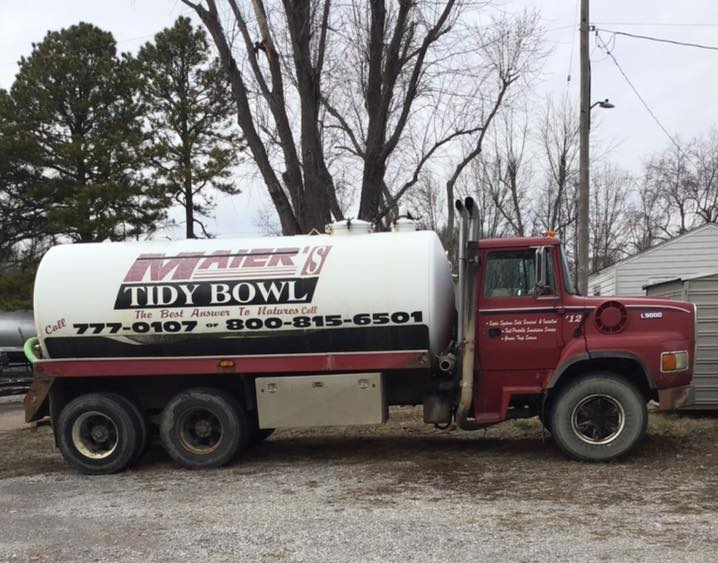 Red Tidy Bowl tanker truck parked on gravel with trees in the background