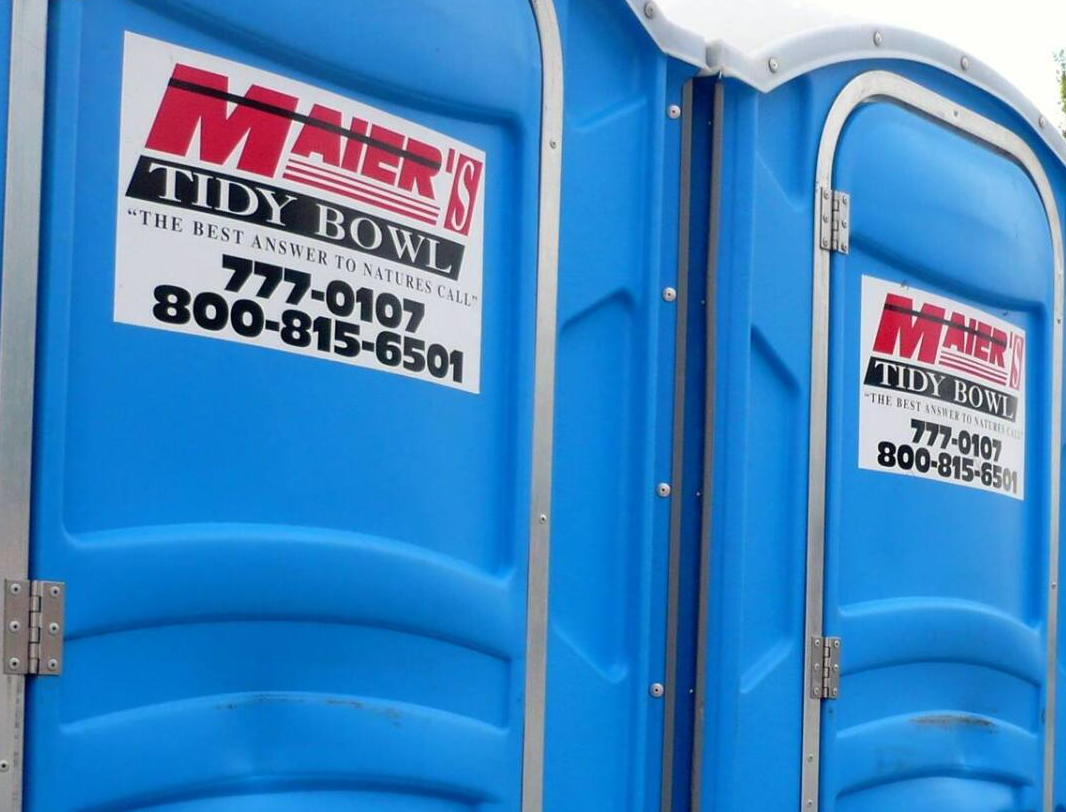 Blue portable toilet with white signs on the doors in an outdoor setting