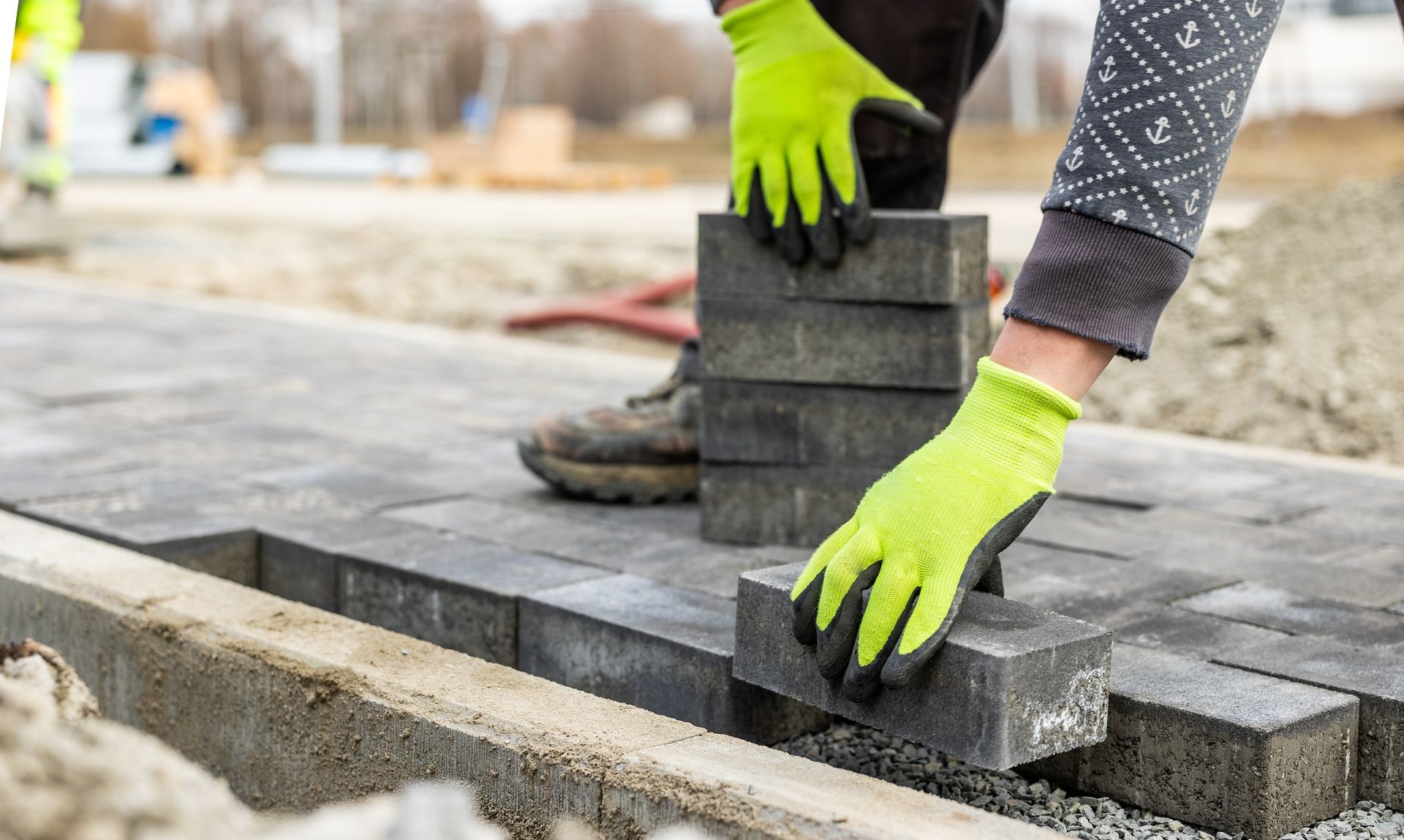 A worker in gloves placing gray interlocking pavers to build a new driveway surface