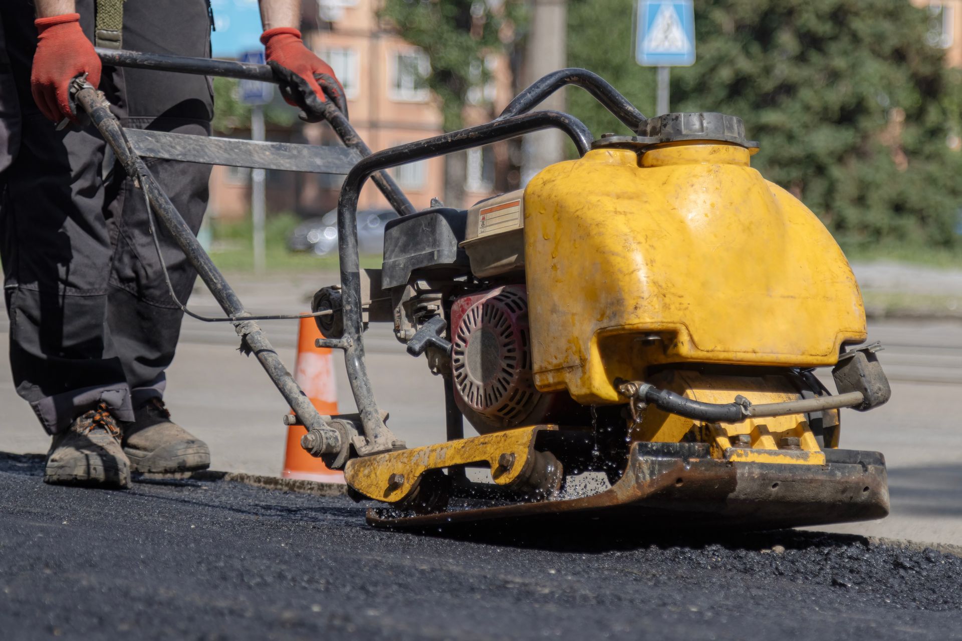 Paving contractor using a plate compactor to tamp fresh asphalt patch