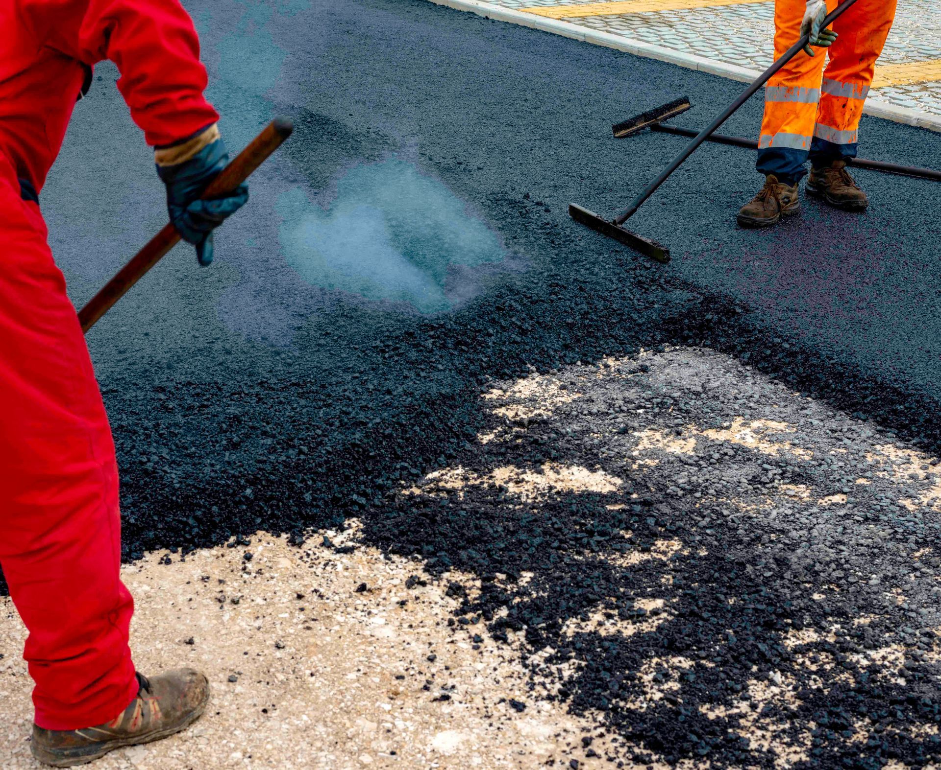 Road workers spreading hot asphalt during pavement repair on a city street.