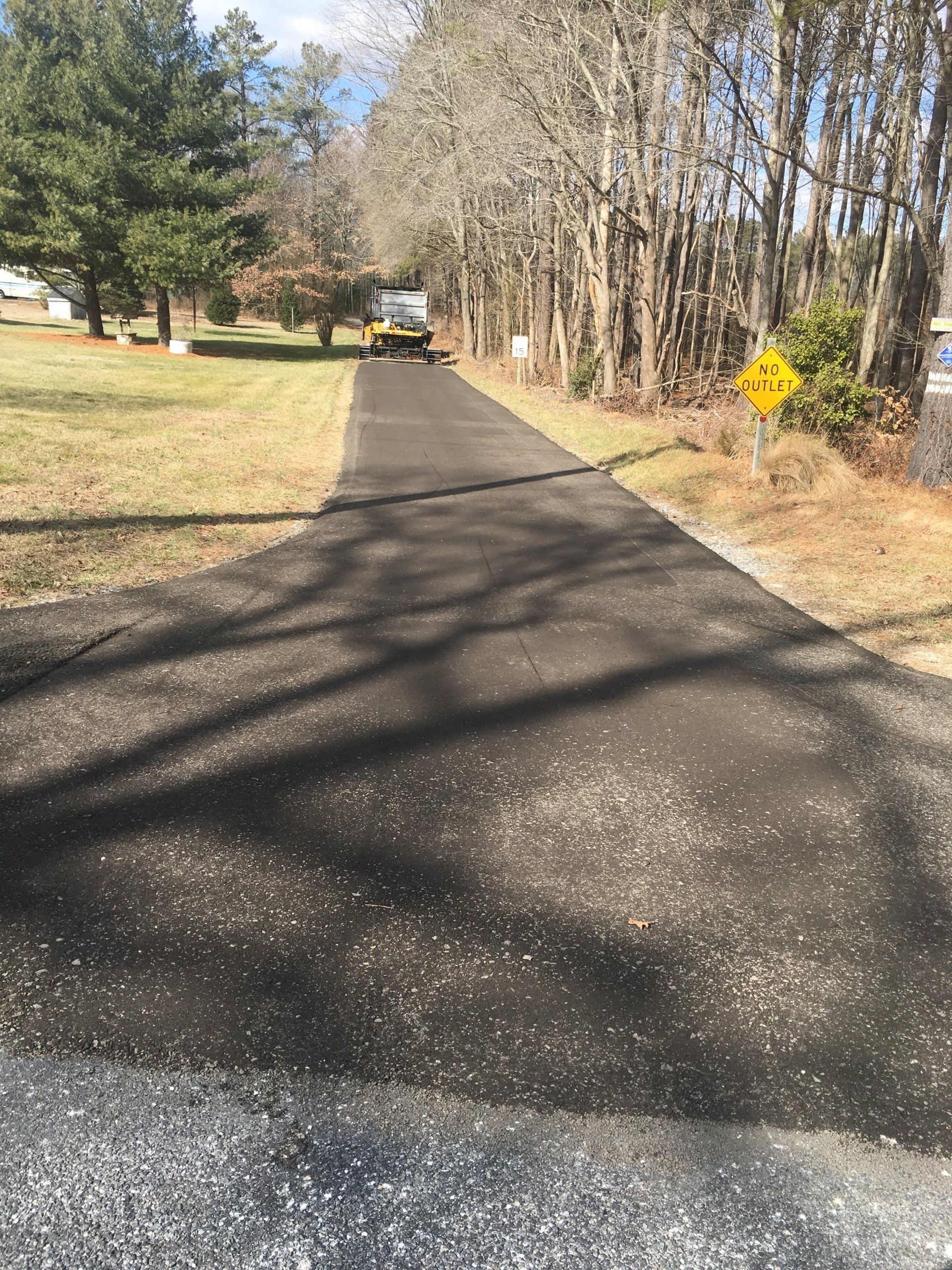 Paved road with a yellow warning sign on the right, trees and a vehicle in the distance.