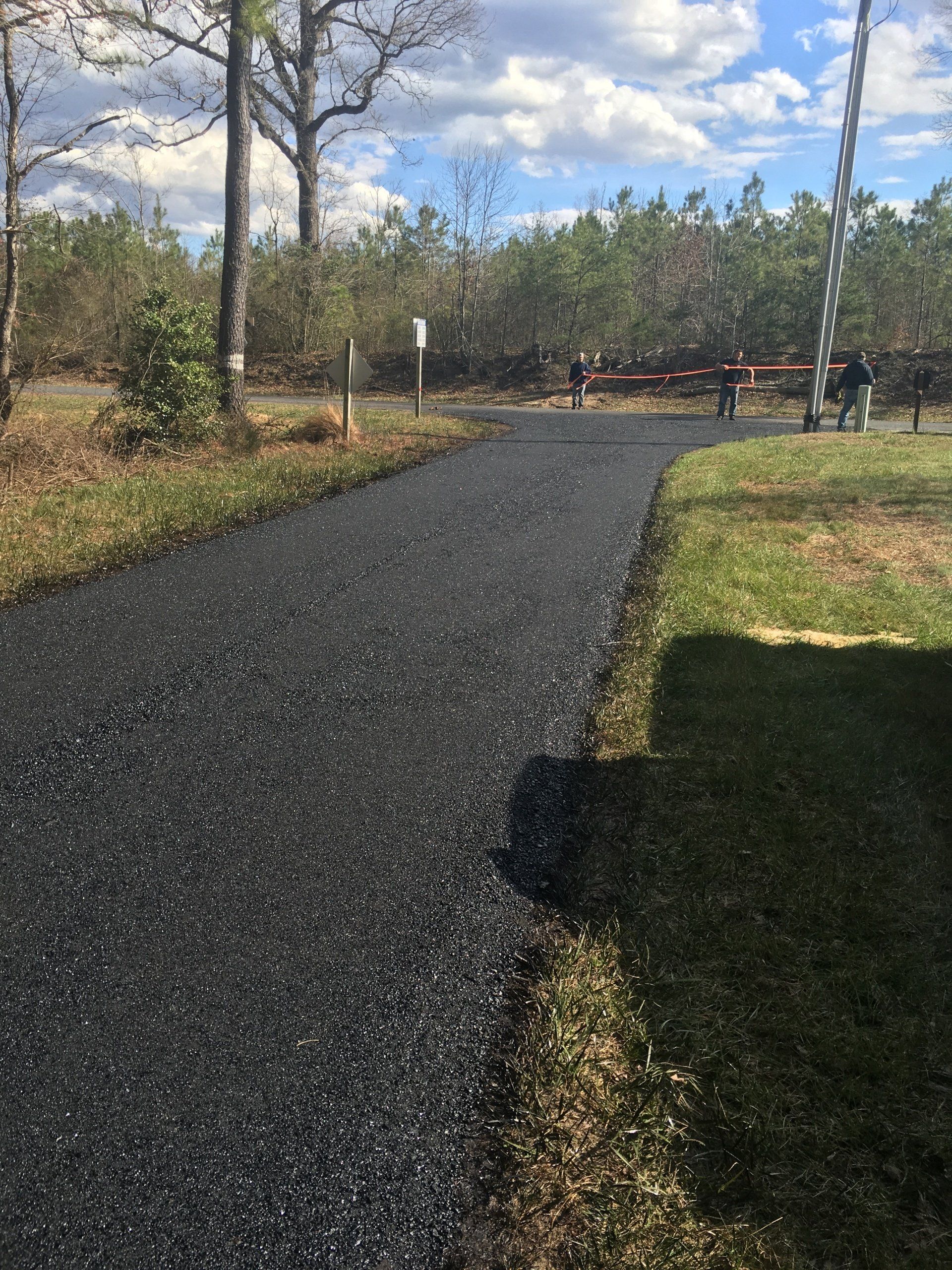 Asphalt path through a park, with trees on either side and people in the distance.