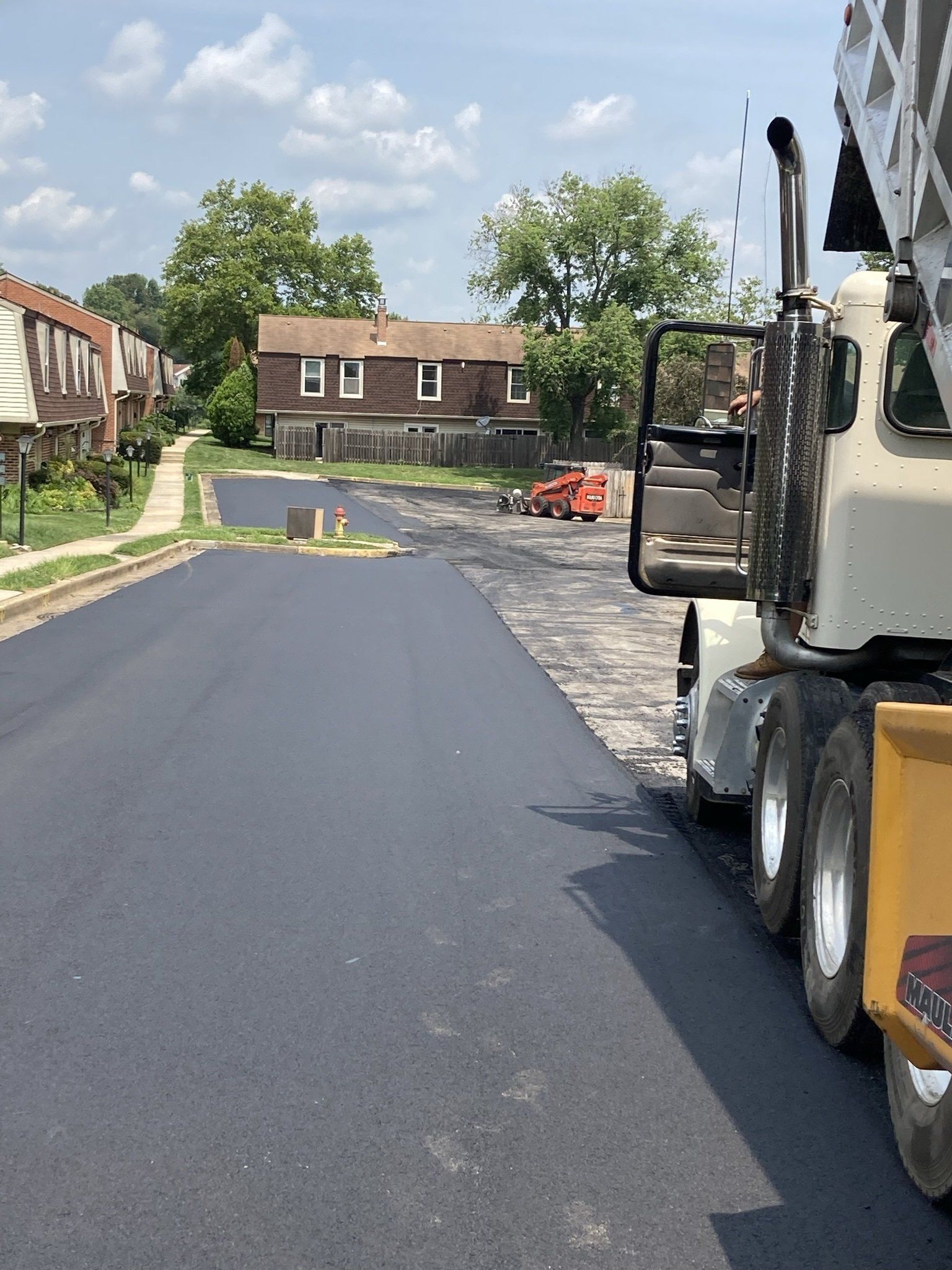 Asphalt paving of a residential street with a concrete truck on the right.