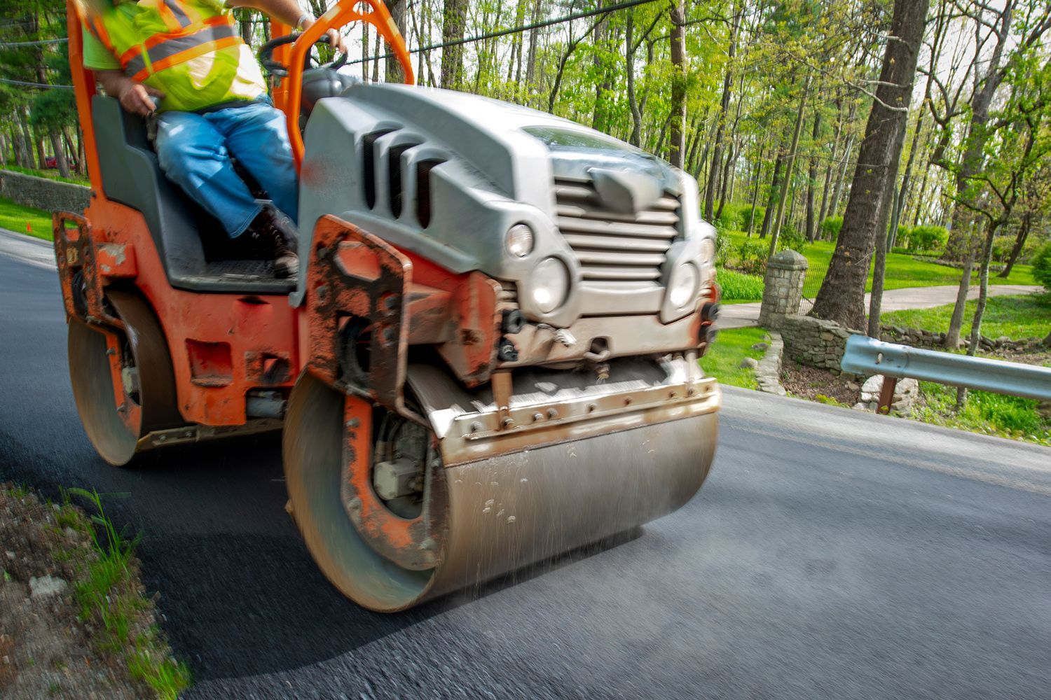 Residential paving contractor operates a road roller to smooth asphalt on a road under construction.