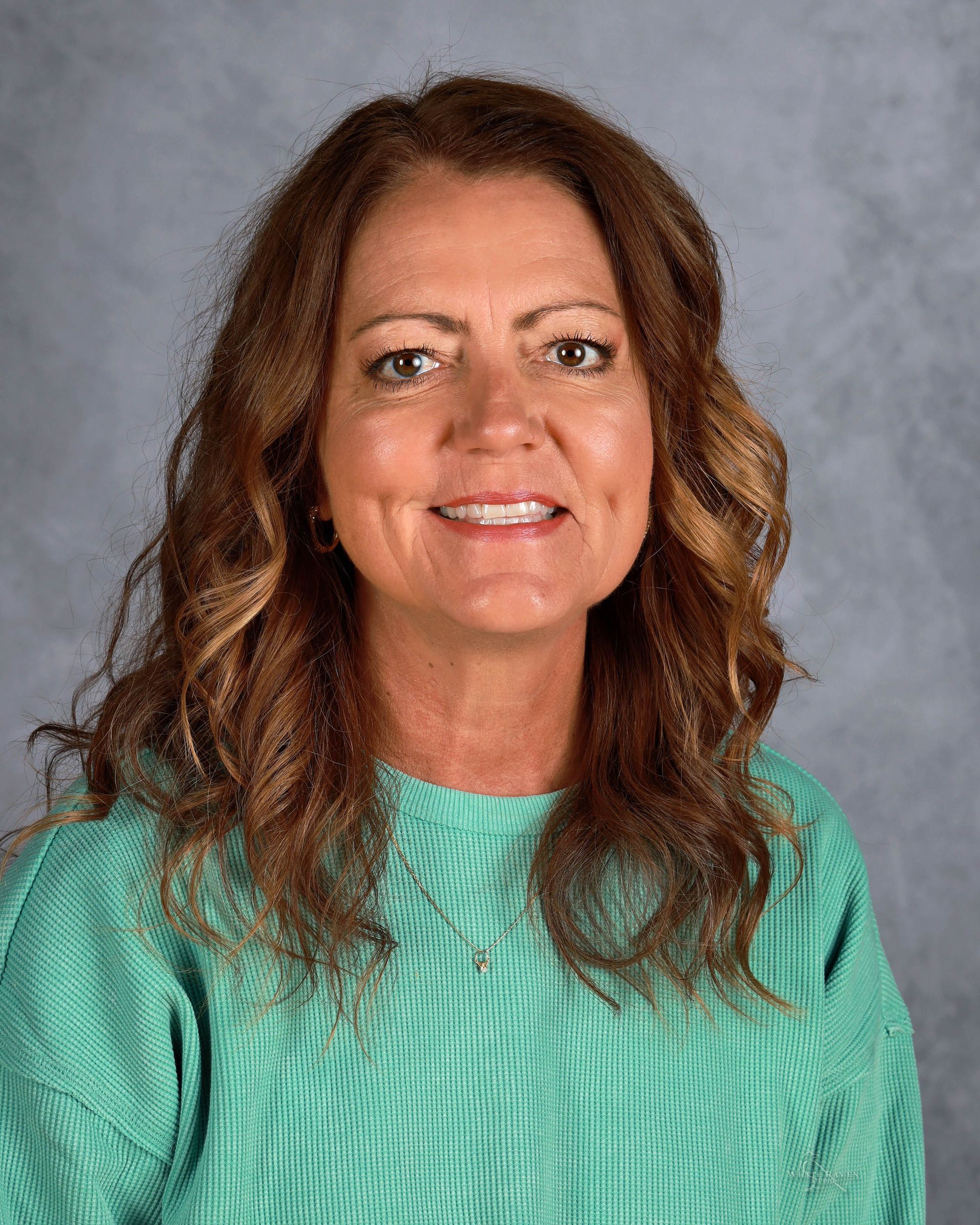 Woman with brown curly hair, smiling, wearing a green sweater, against a blue background.