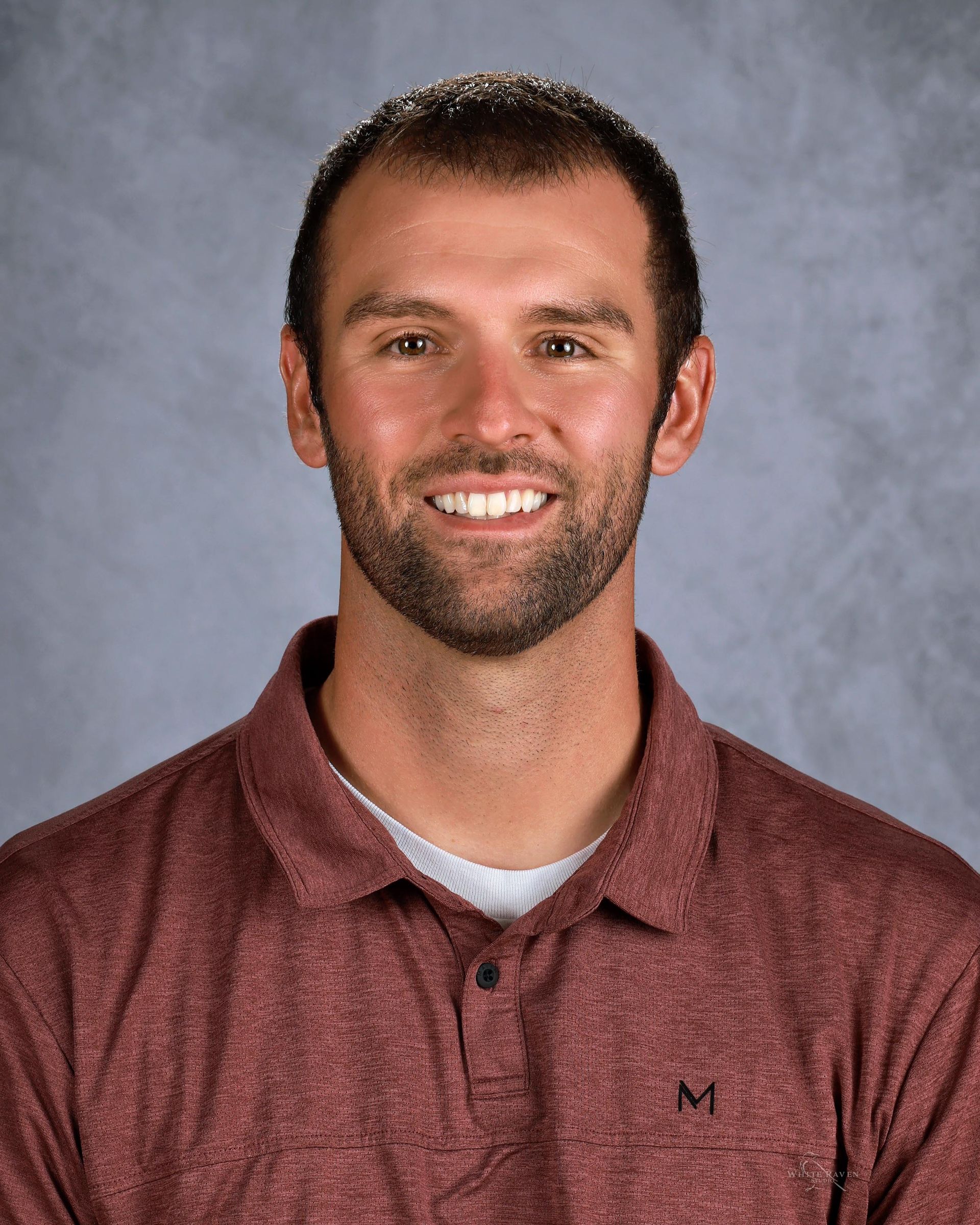 A man with a beard smiling, wearing a maroon polo shirt.
