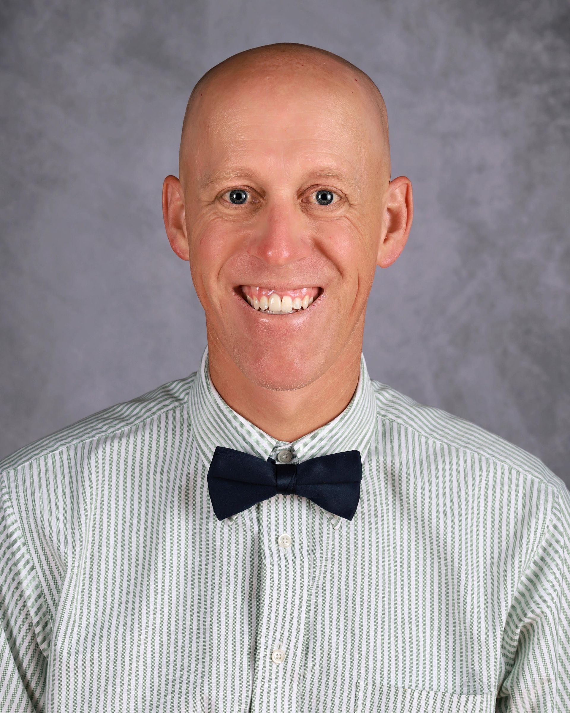 Bald man smiling, wearing a blue bow tie and striped shirt.